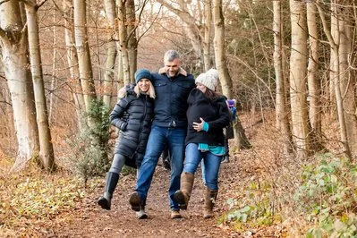 Three people walking together on a forest trail in autumn, wearing winter clothing and smiling.