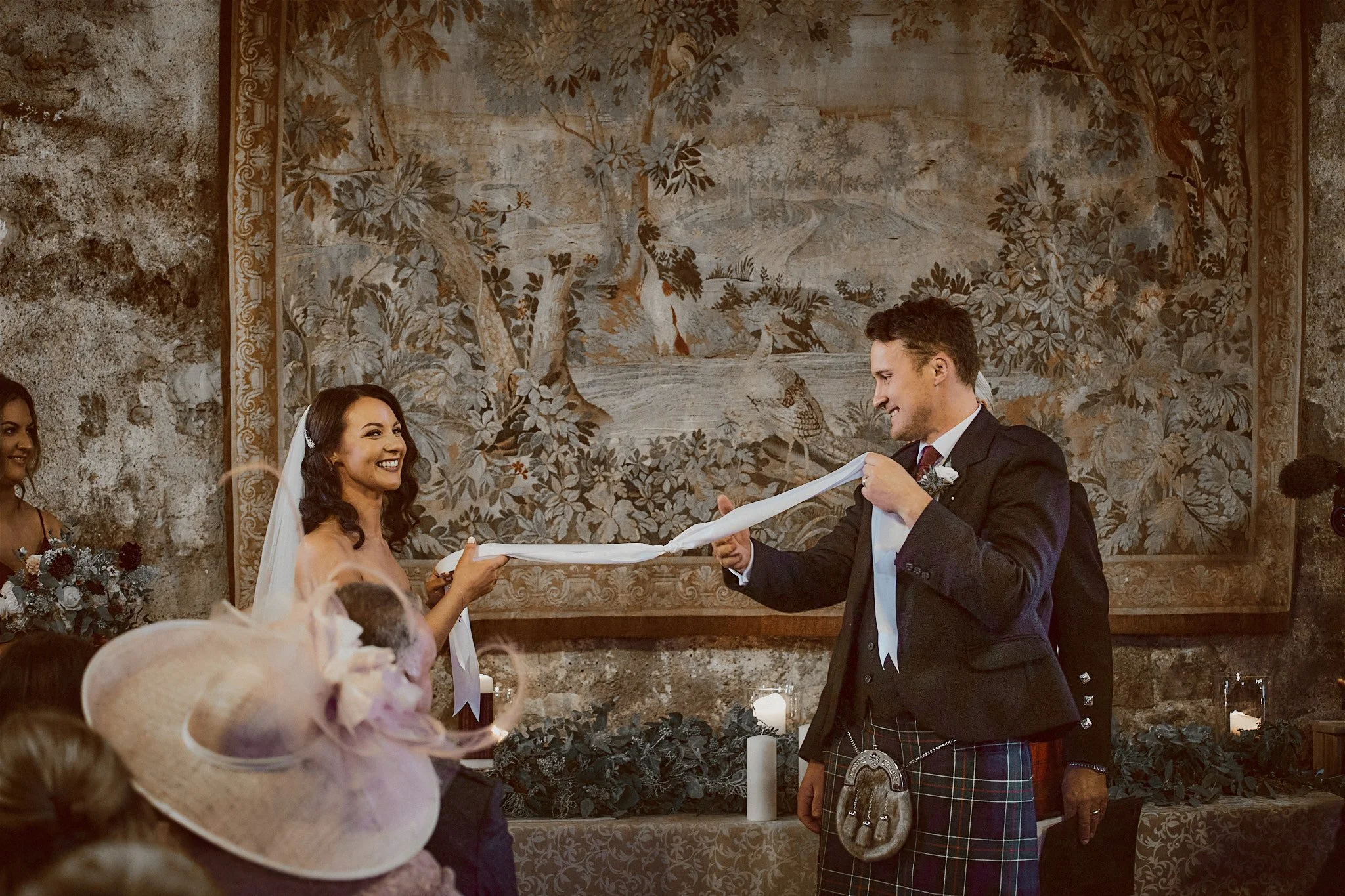Couple performing handfasting ceremony at wedding in rustic setting.