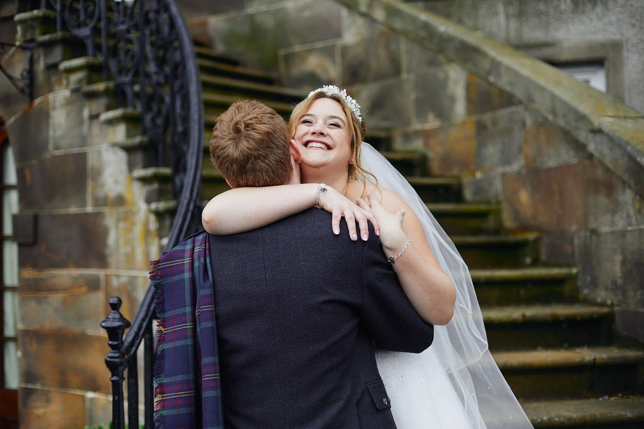 Bride embracing groom in front of stone staircase.
