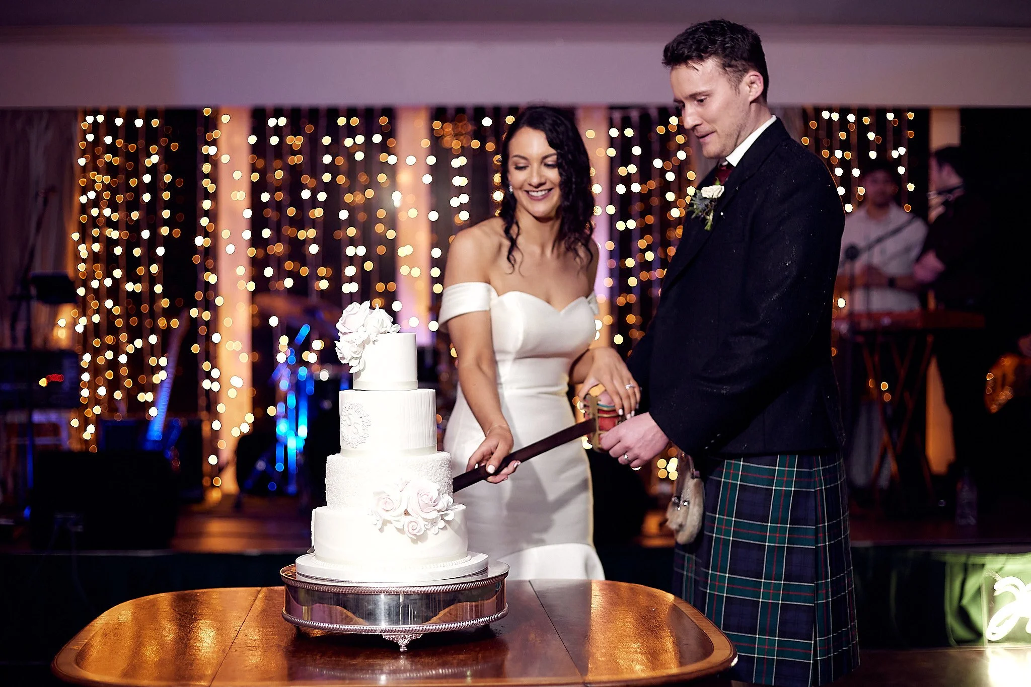 Bride and groom cutting wedding cake with lights in background