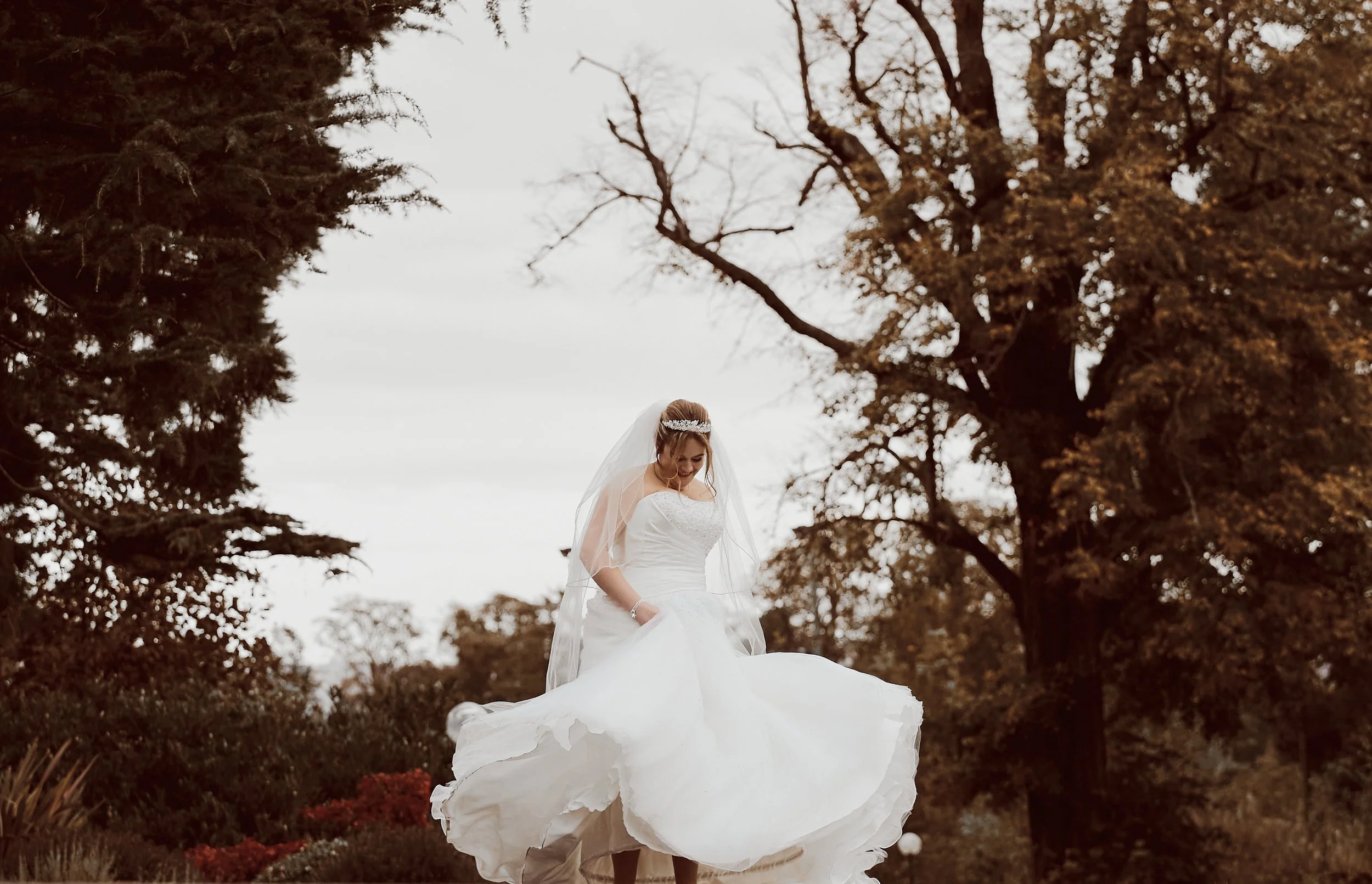 Bride in a white wedding dress walking outdoors, surrounded by trees in autumn.