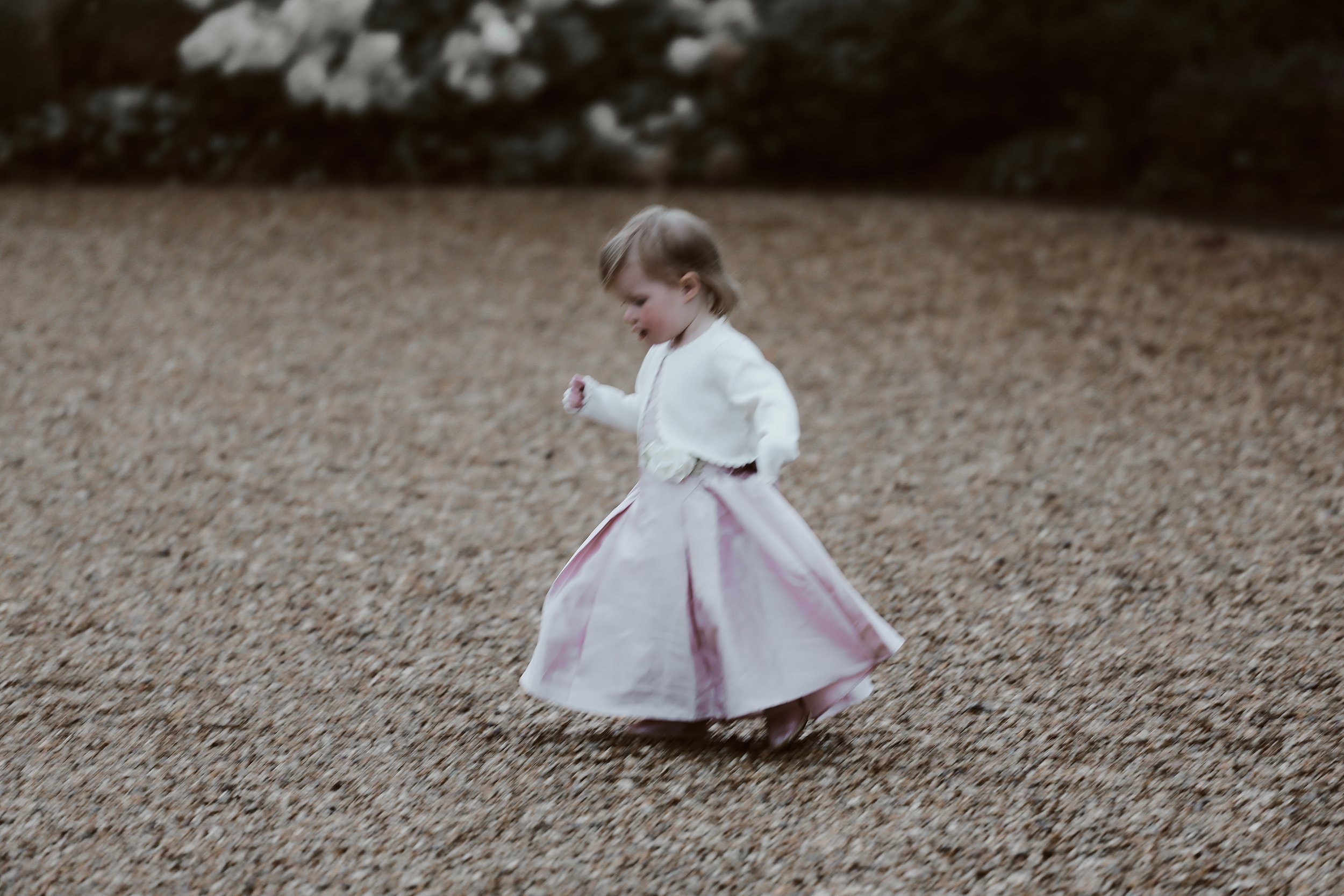 Young child in pink dress and white cardigan running on gravel path.