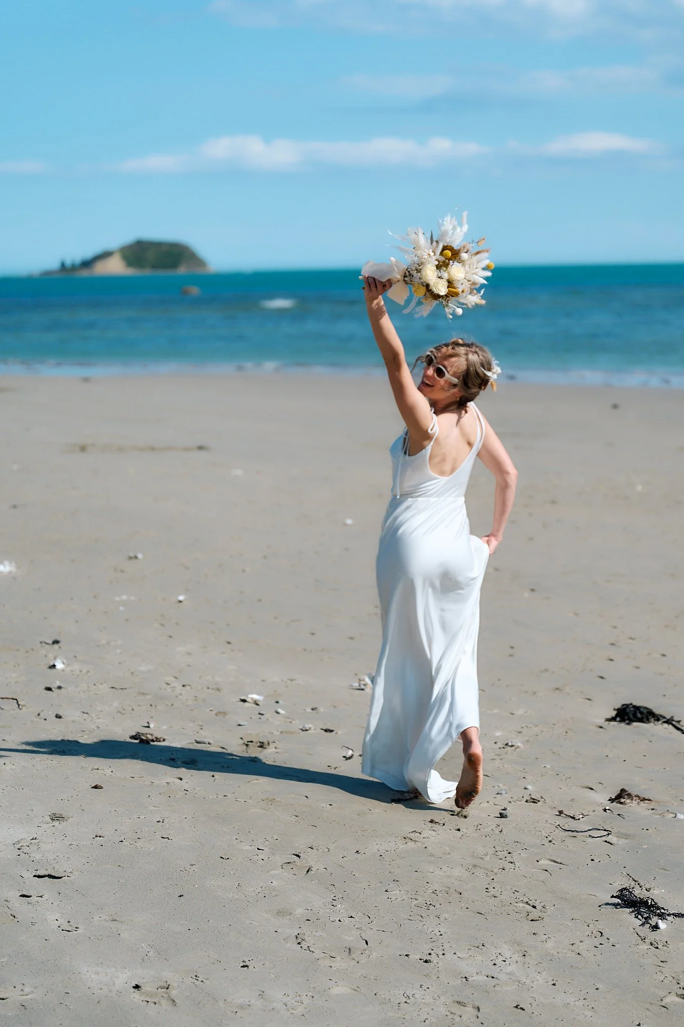 Woman in white dress holding bouquet, walking on beach