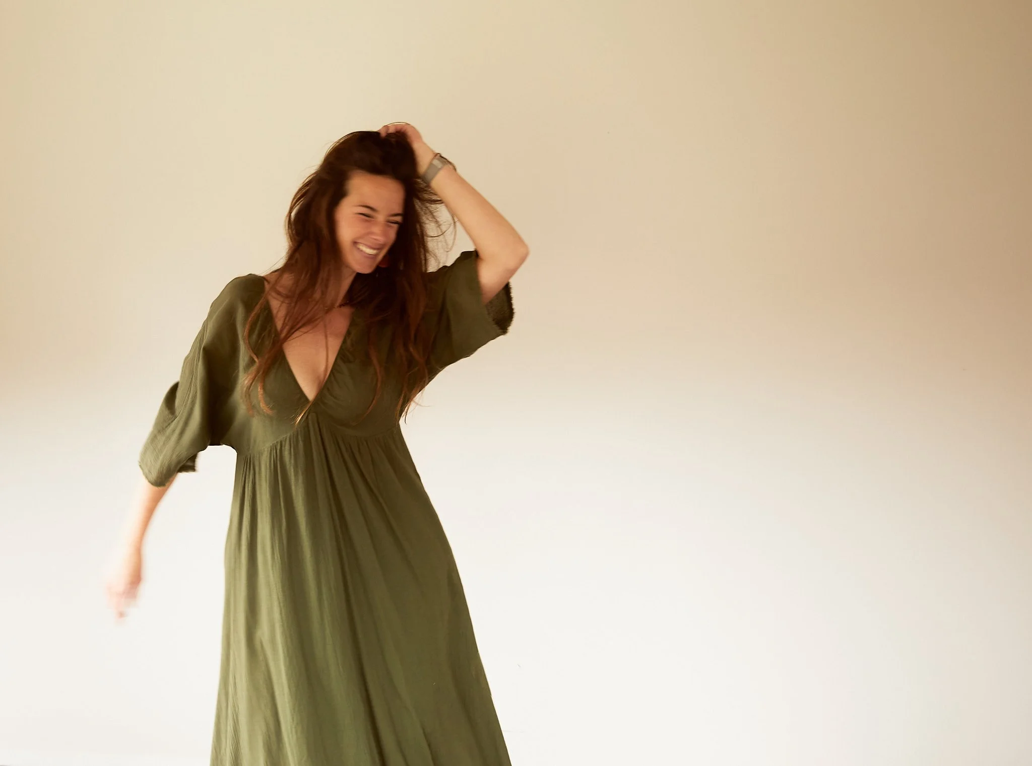 Woman in a green dress smiling and posing against a plain background.