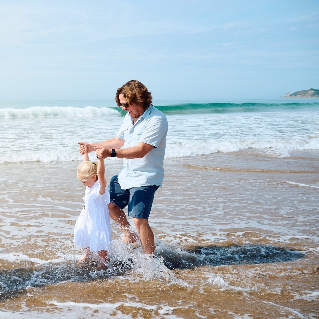 Family walking on a sandy beach with a dog, near the ocean, under a partly cloudy sky.