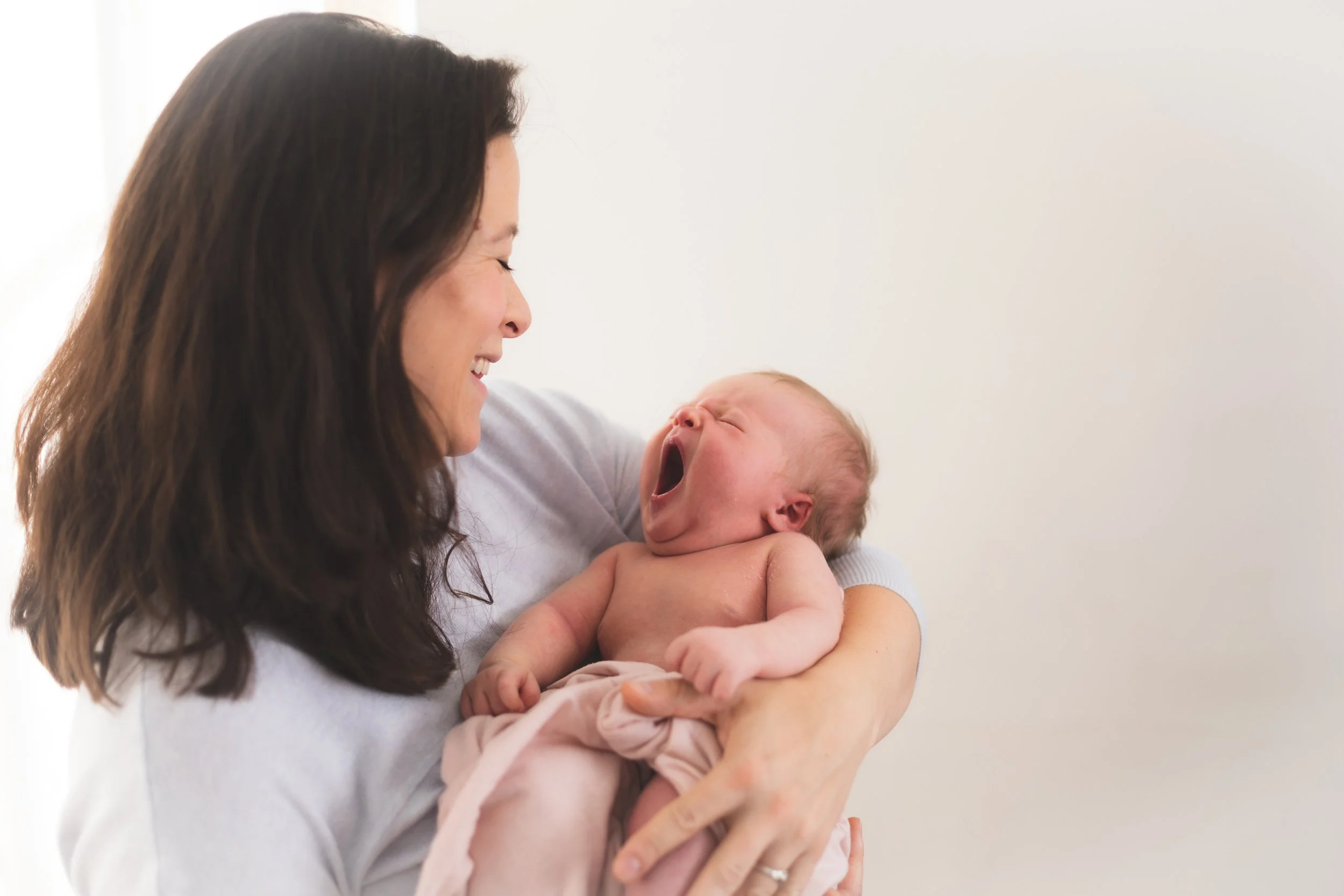 Smiling woman holding a yawning baby.