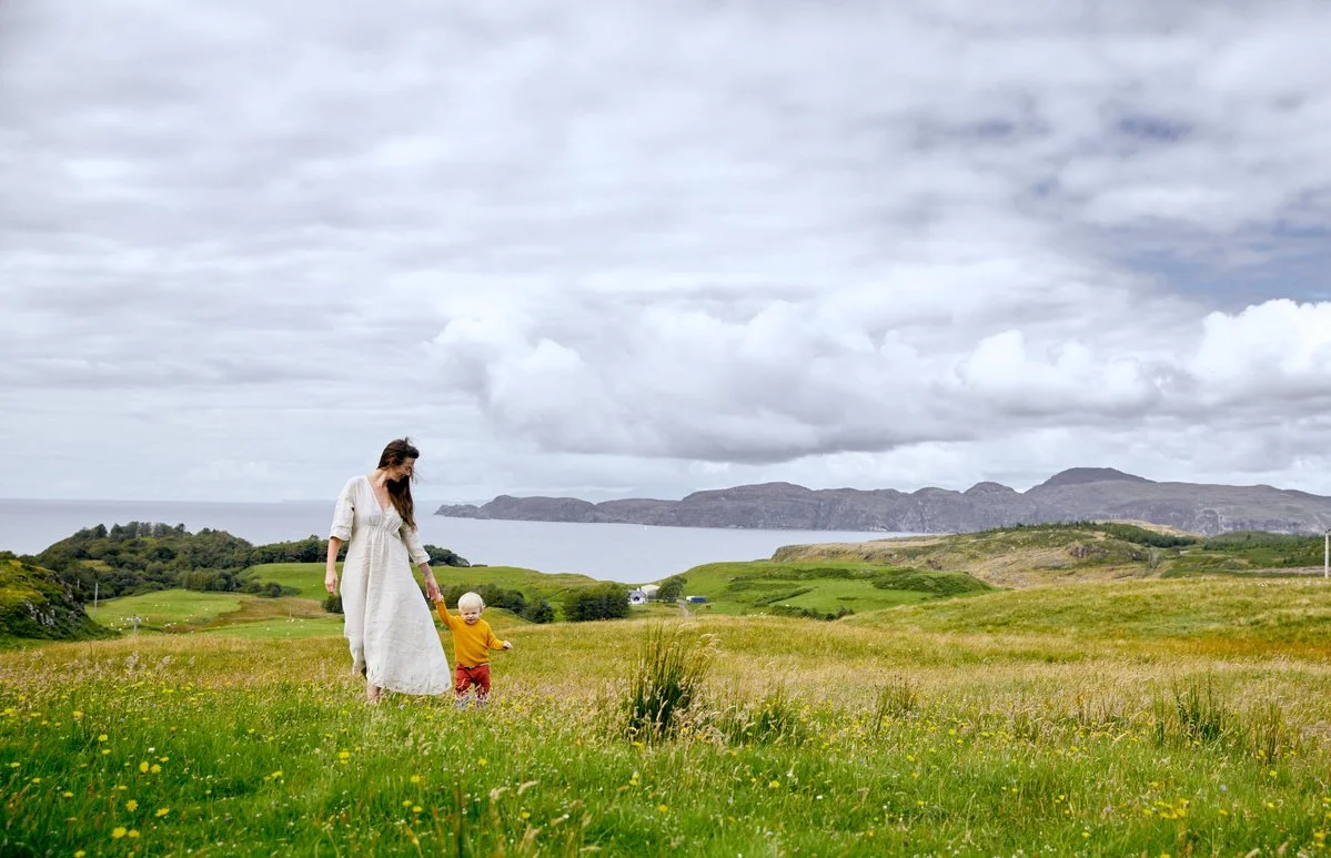 Woman and child walking in a green meadow with mountains in the background.