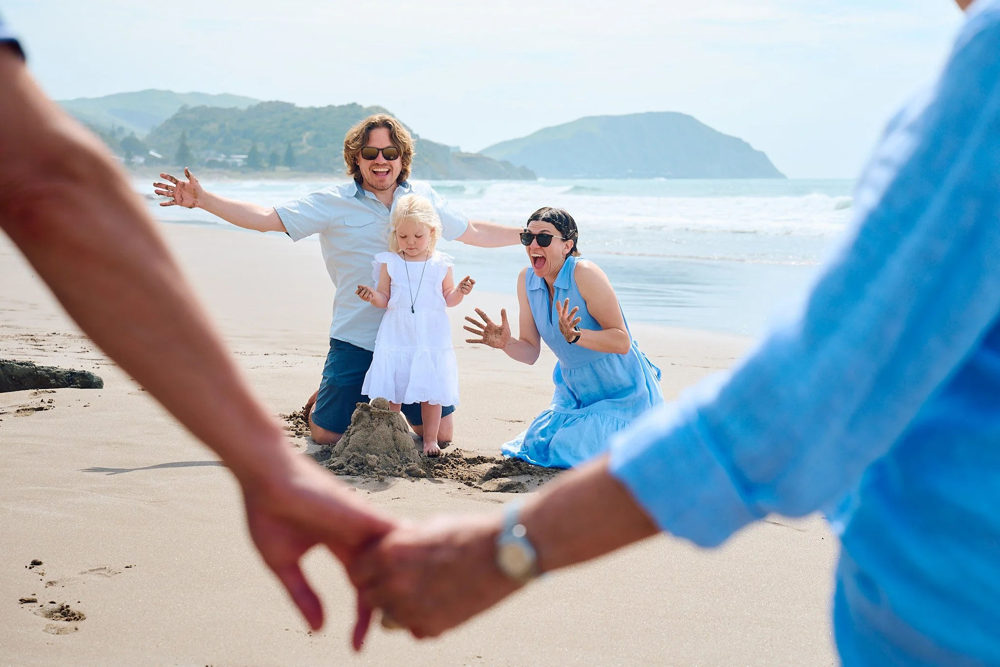 Family playing on a beach, building sandcastles, with mountains in the background.