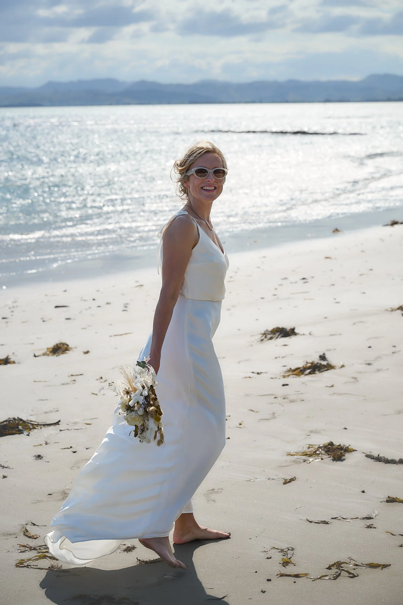Woman in a white dress holding a bouquet on a beach