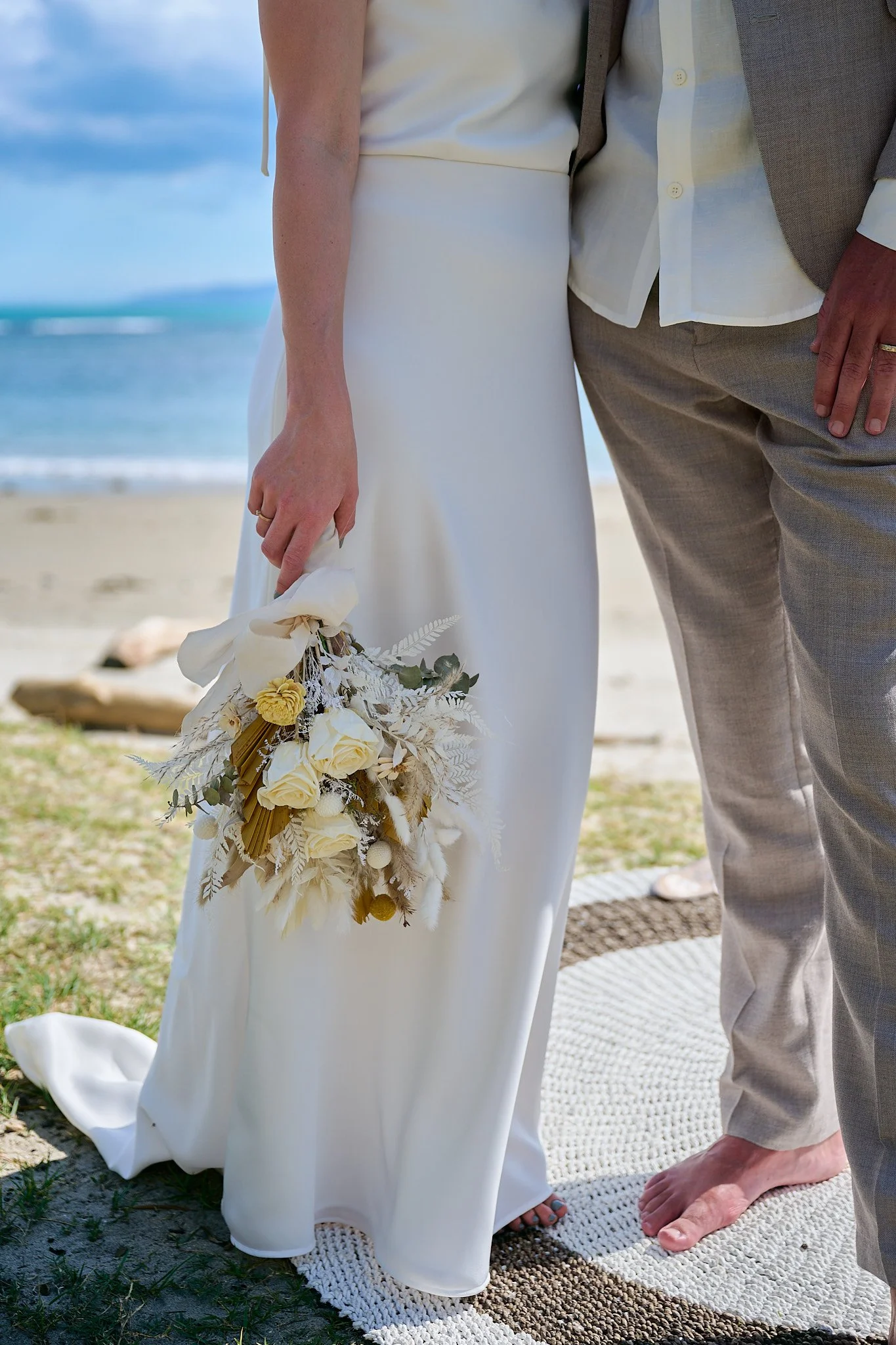 Bride holding bouquet next to groom on beach