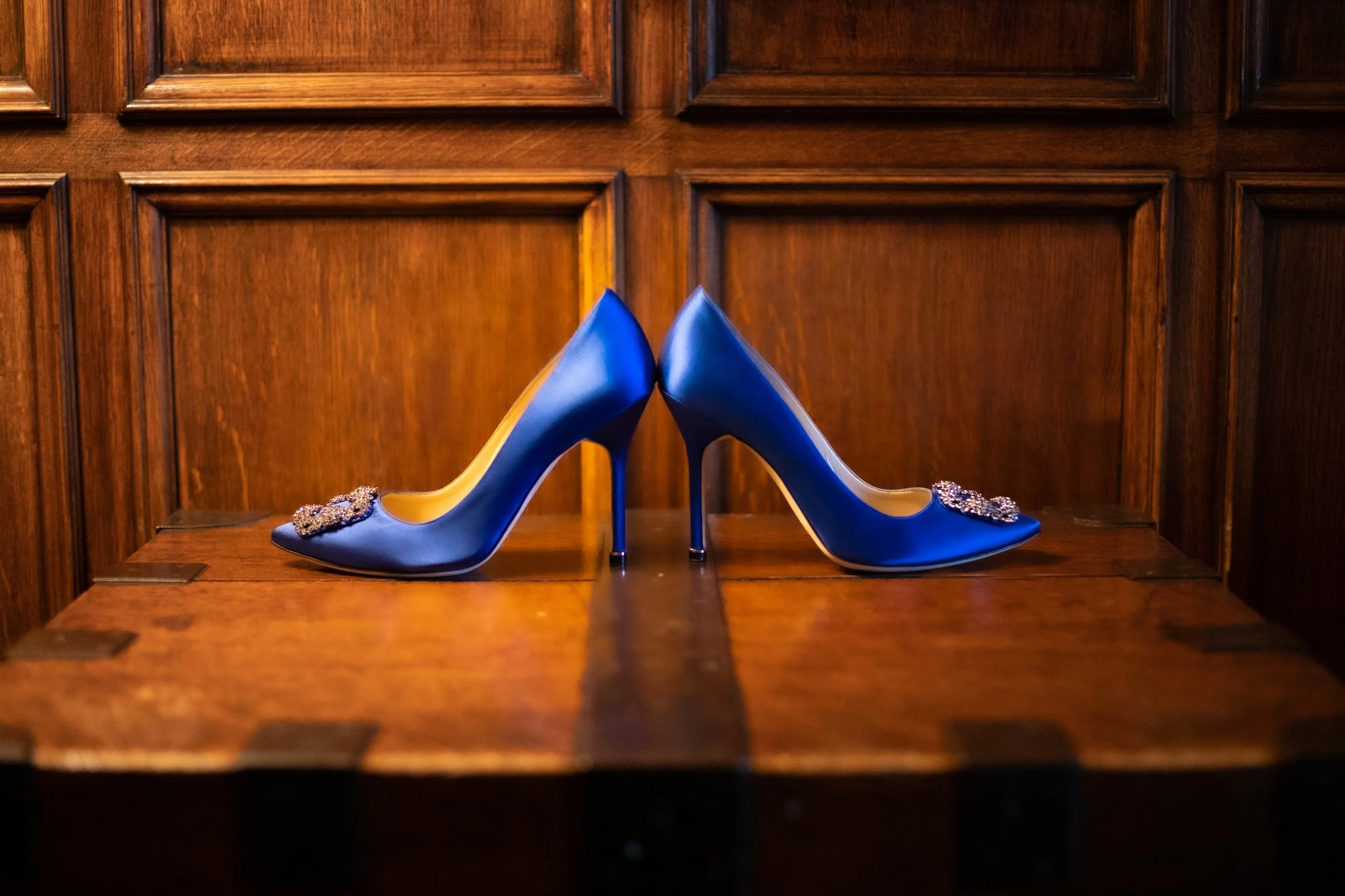 Two blue high-heeled shoes with embellishments on the toes, set against a wooden background.