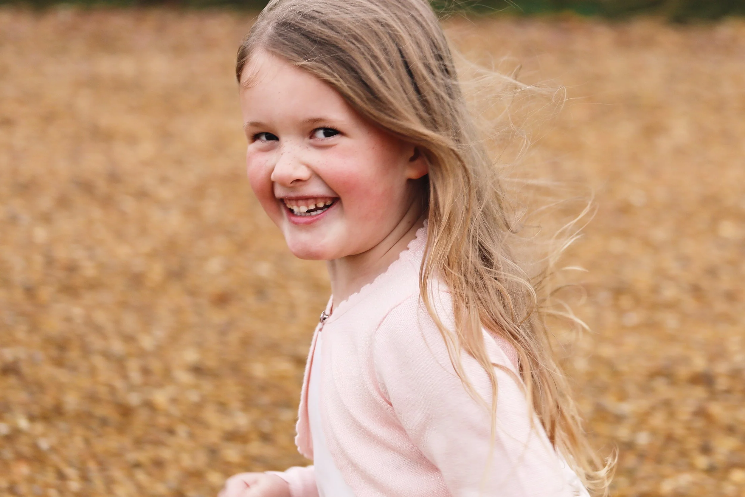 Smiling girl with long blonde hair and pink jacket outdoors