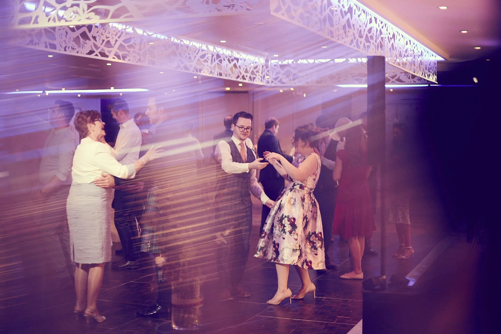 People dancing at a formal event with a floral ceiling decoration.