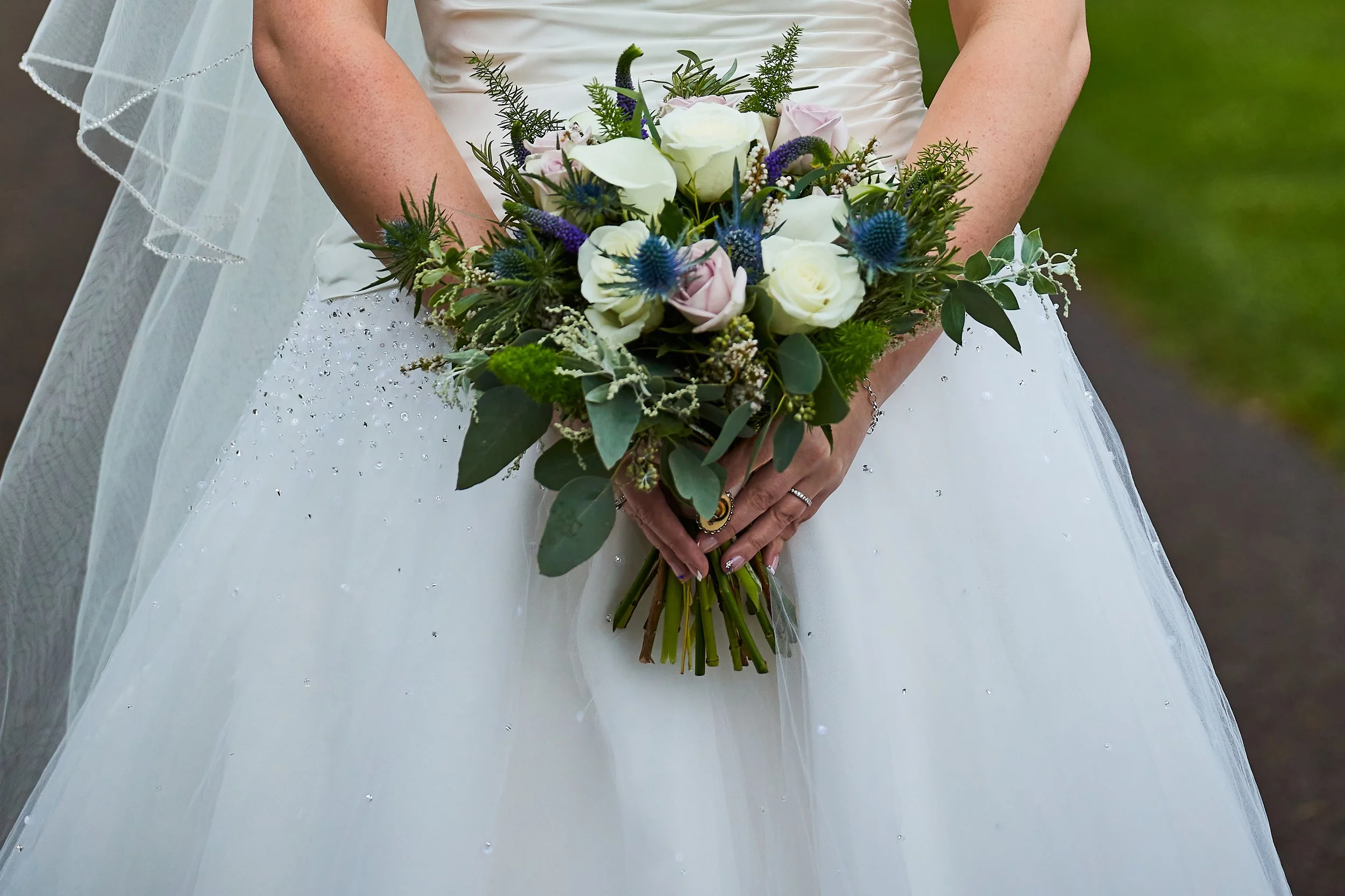 Bride holding a bouquet of white roses and greenery, wearing a white wedding dress with veil.