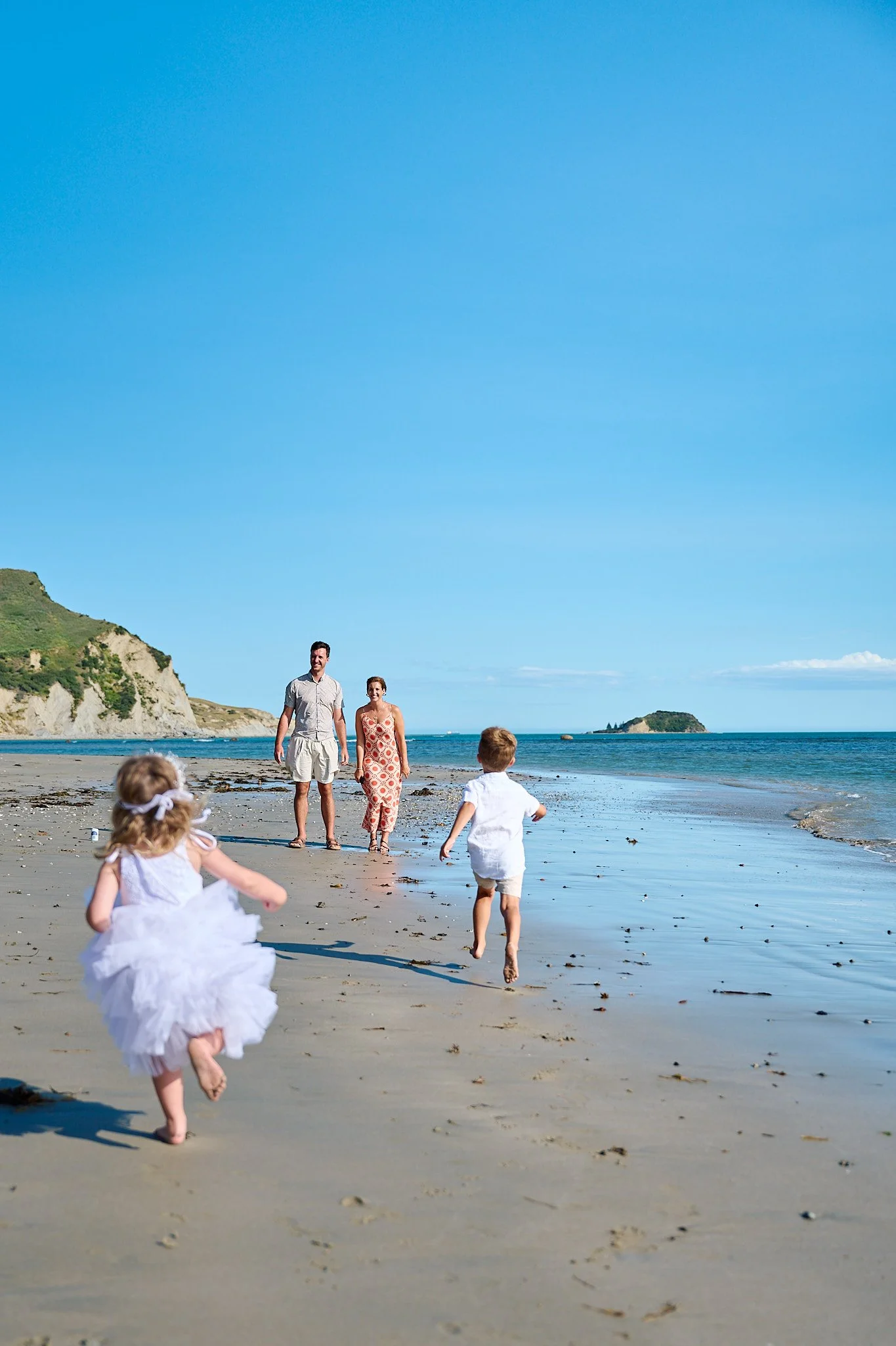 Family walking and children running on a sunny beach with blue sky and ocean
