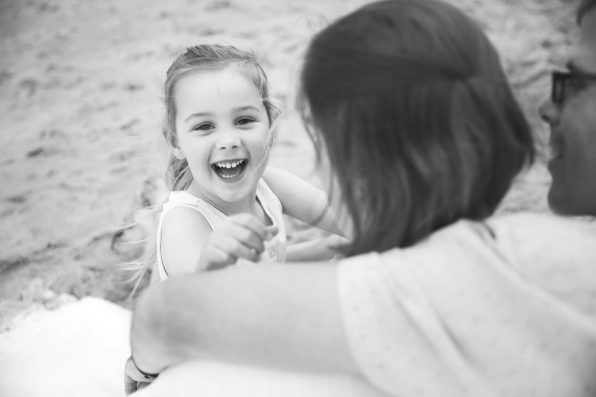 Black and white photo of a smiling young girl with adults at the beach.