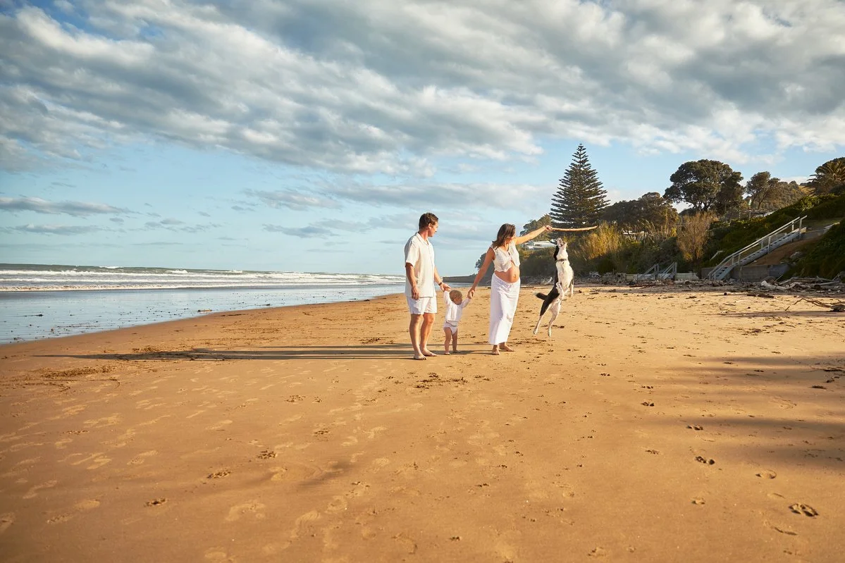 Family with a dog walking on a beach under a cloudy sky.