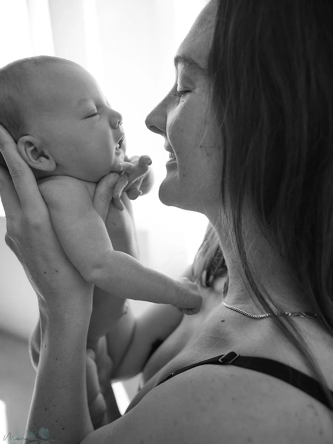 A woman smiling and holding a newborn baby close to her face in a black and white photo.