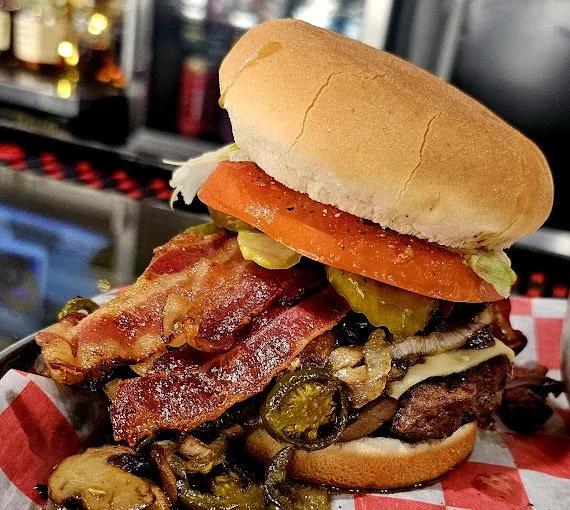 Bacon cheeseburger with lettuce, tomato, pickles, grilled mushrooms, and a bun.