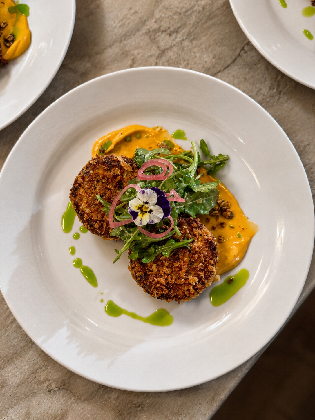 Crab cake appetizer with arugula, pickled shallots, and edible flower