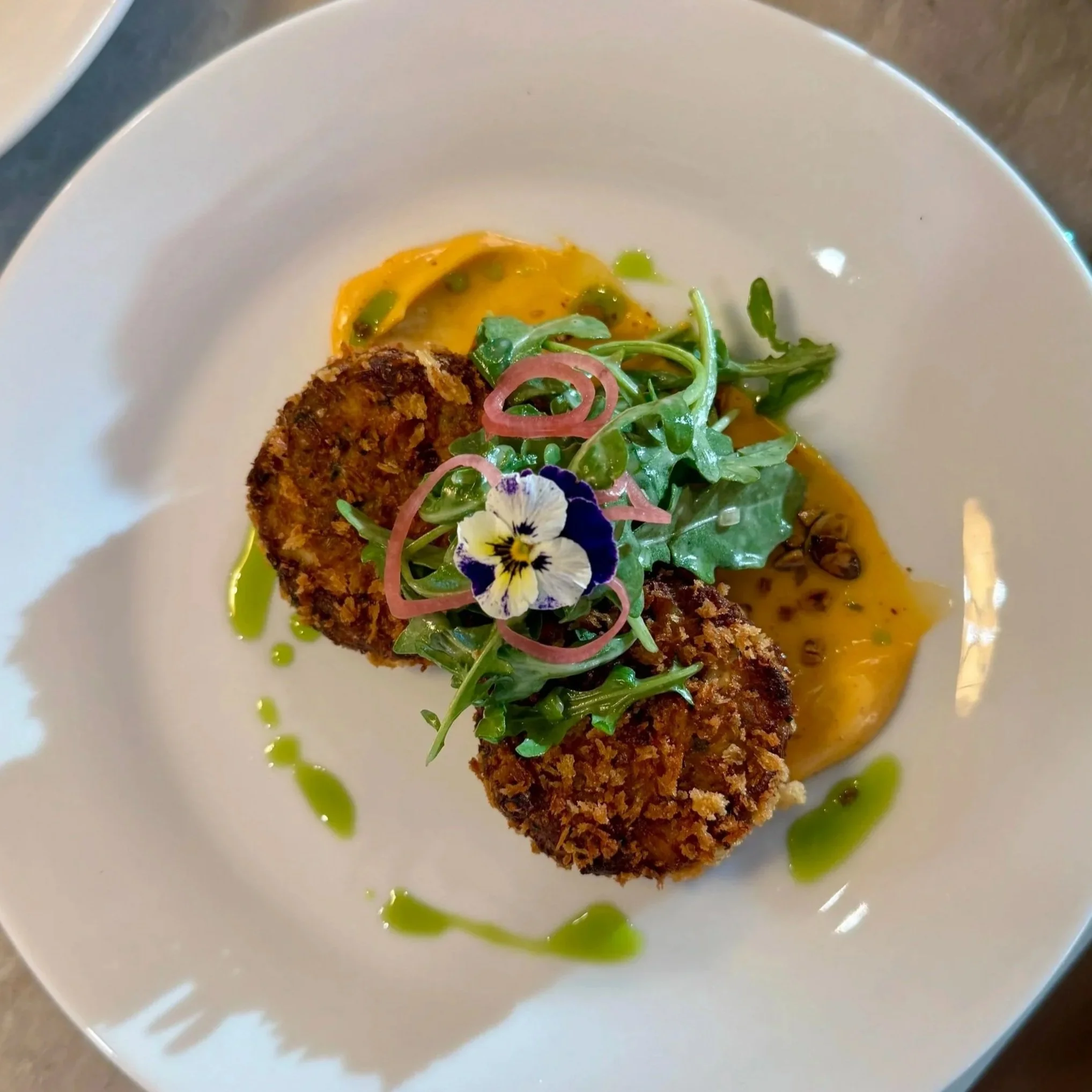 Plated crab cakes with dressed greens and edible flower