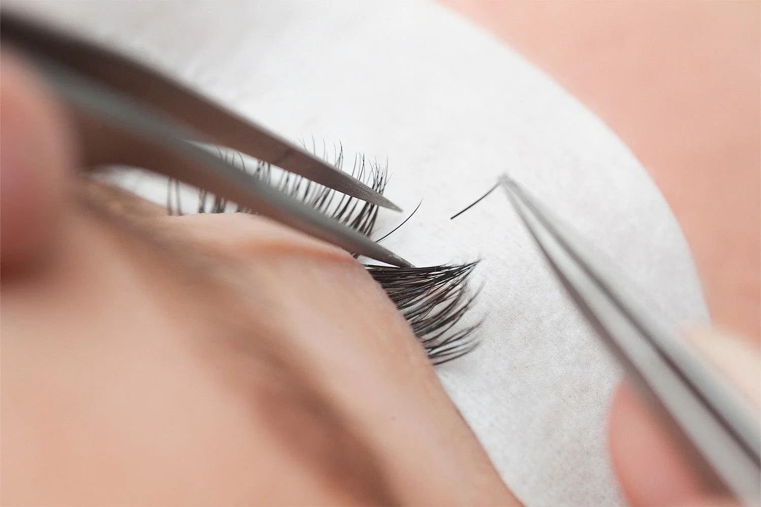 Close-up of eyelash extension application with tweezers and a person's eye.