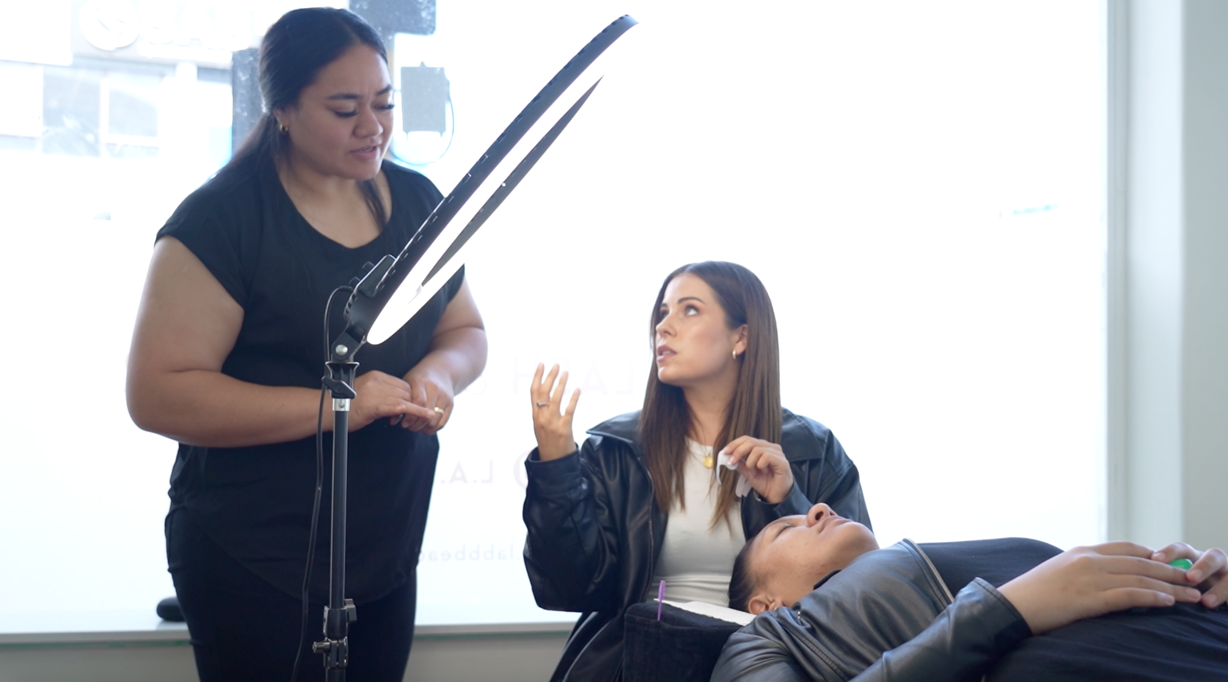 A woman lying on a beauty chair having her lashes done. Trainer Nicole Rutherfurd showing a eyelash extension student how to do eyelash extensions.
