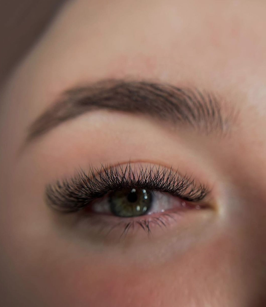 Close-up of a person’s eye with long, curled eyelashes and a well-defined eyebrow.