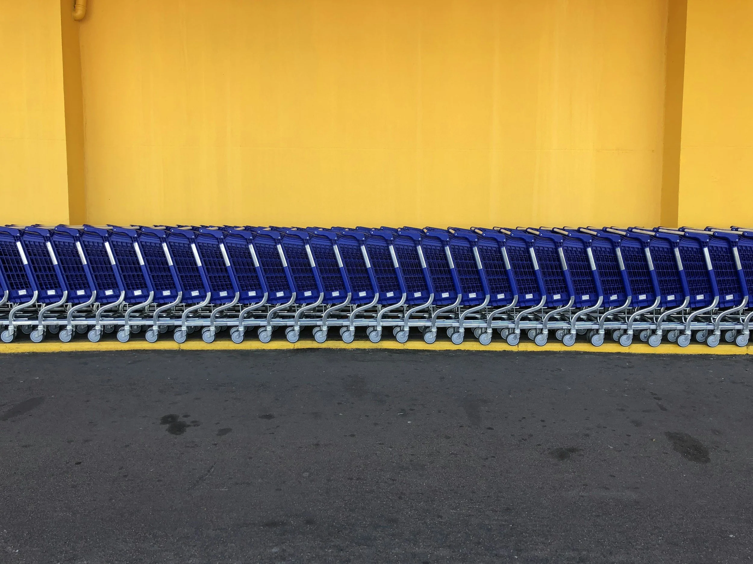 Row of blue shopping carts lined up against a vibrant yellow wall in a parking lot.
