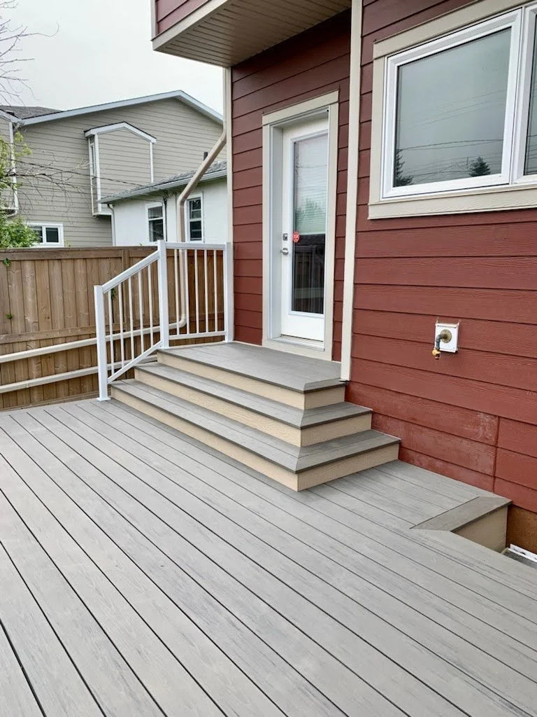Wooden deck with stairs leading to a back door, red house siding, window, and water hookup near the door.