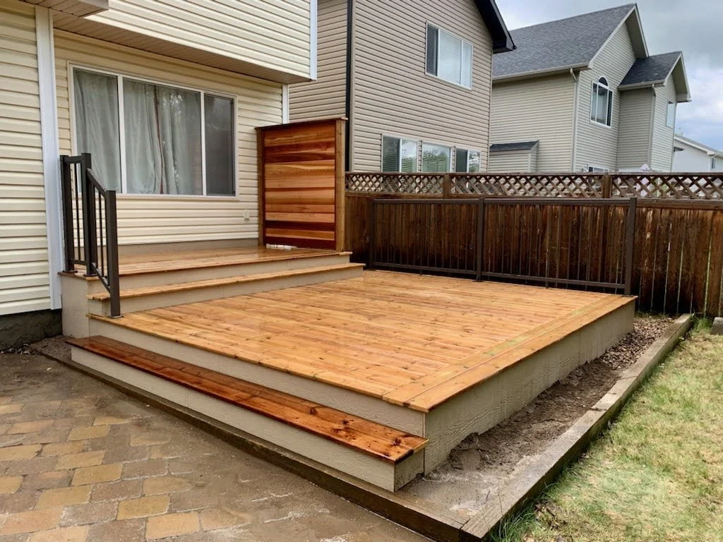New wooden deck with stairs attached to a house, fenced in with a multi-level railing.