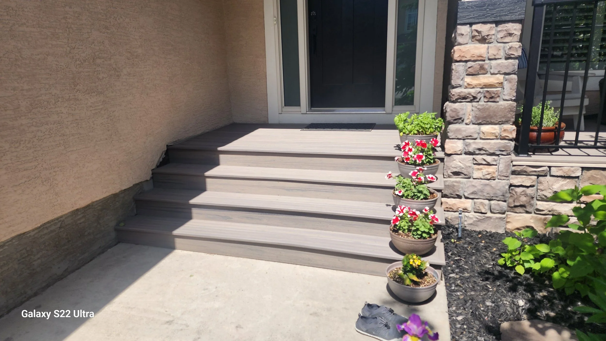 Front porch with wooden stairs, potted flowers, and a sliding glass door.