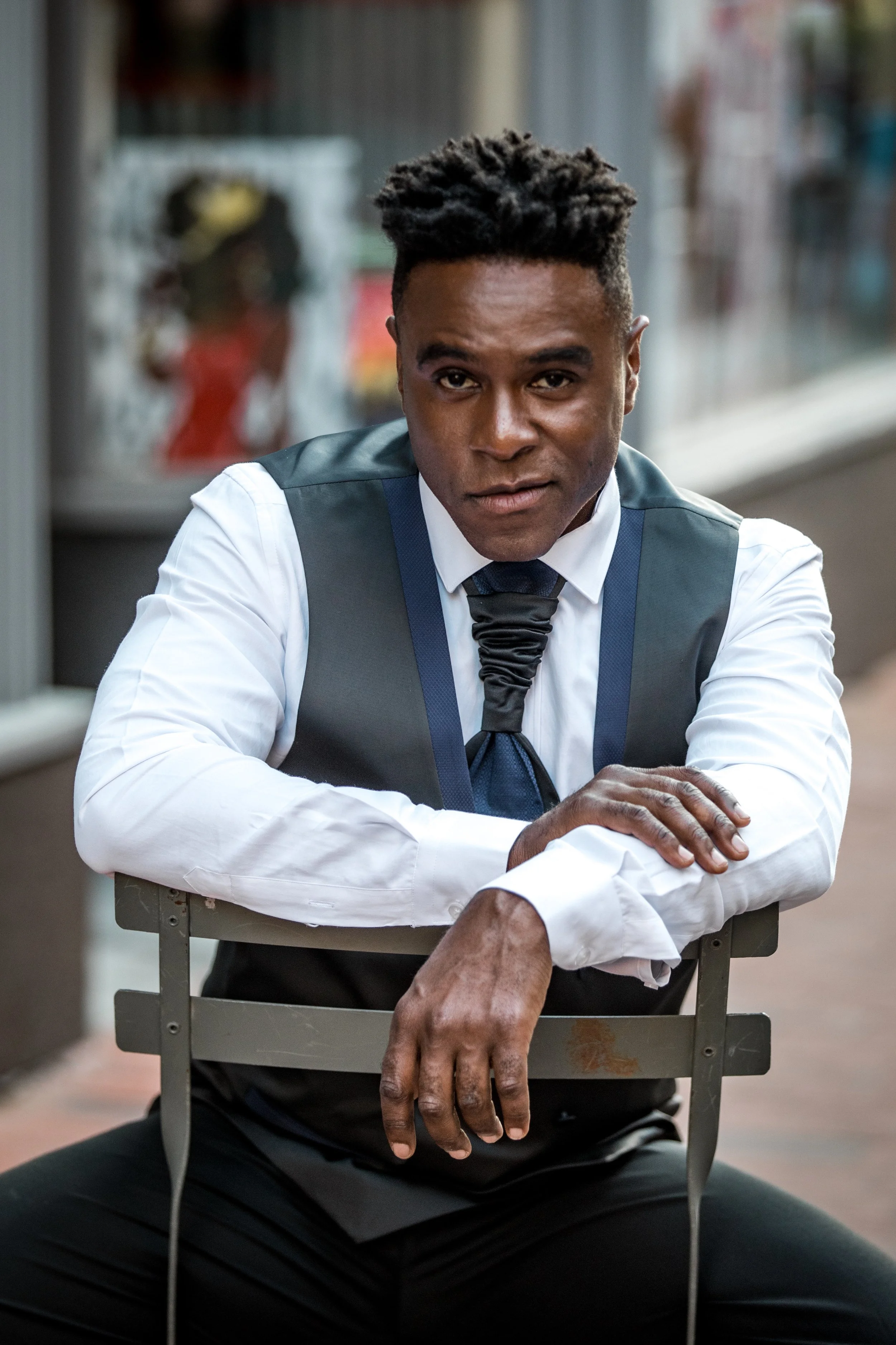 Portrait of Julius P. Williams III, a young African American man with short, curly hair, wearing a white shirt, black vest, and tie, in an indoor setting with blurred background.