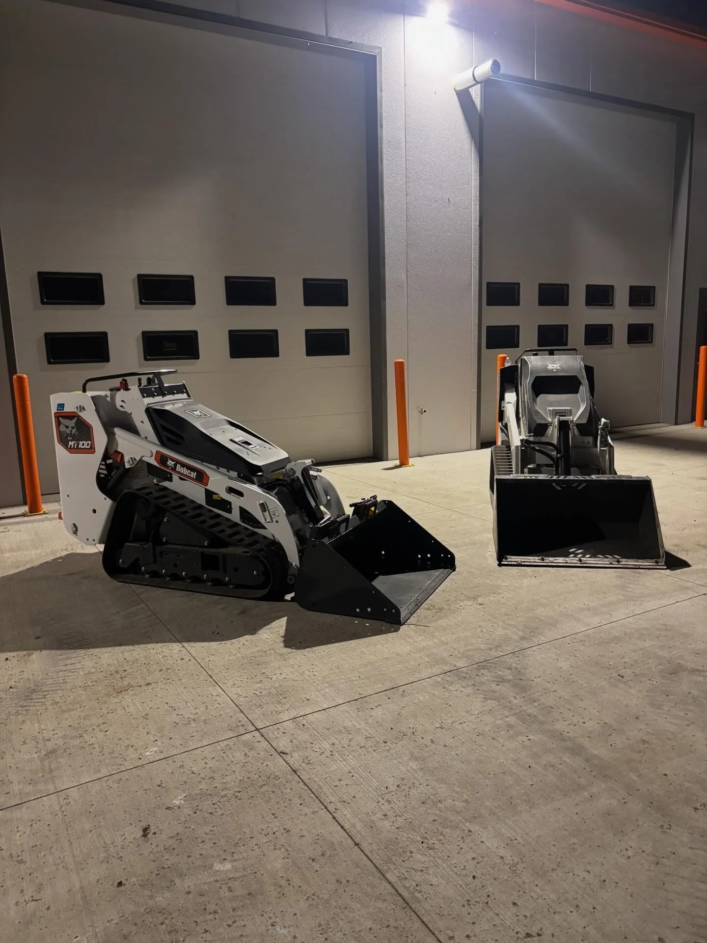 Mini skid steer parked in front of garage doors at night