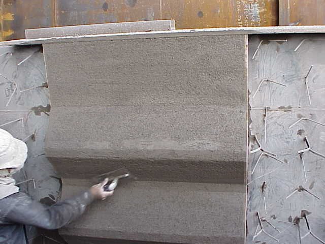 Dos trabajadores en equipo usando casco, gafas y máscara de protección, trabajando en una Estructura de acero con anclajes refractarios en un sitio de construcción.