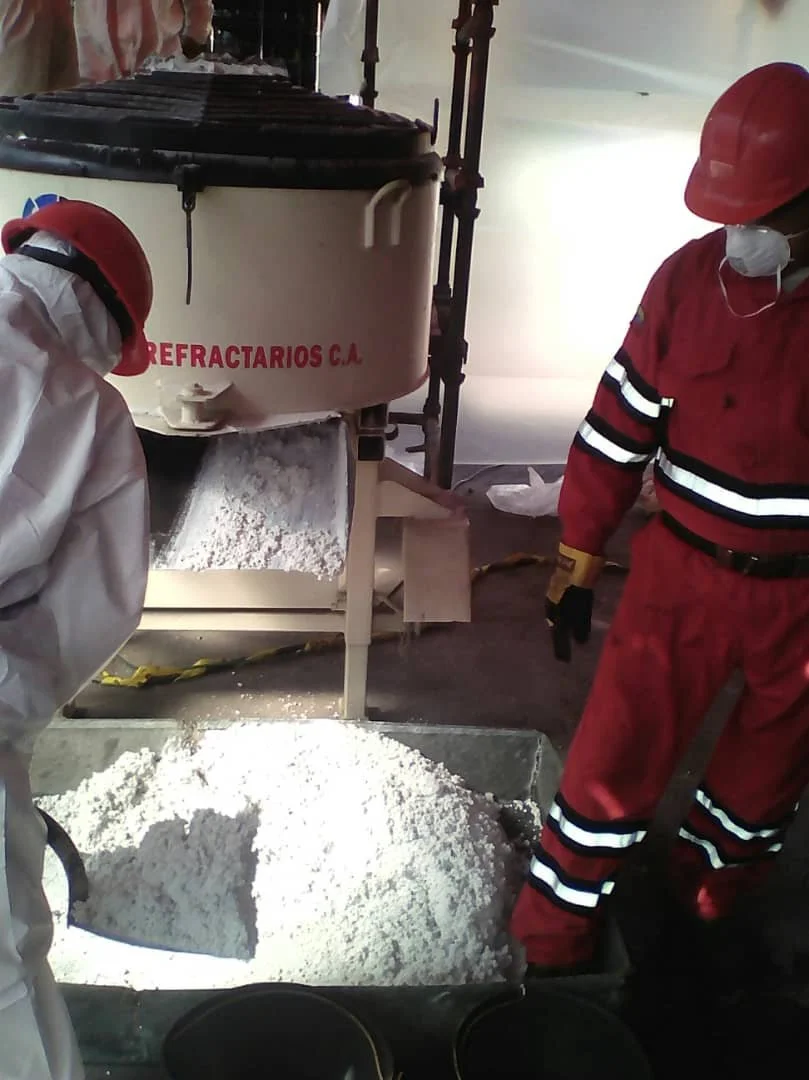 trabajadores con cascos y mascarillas operando una mezcladora