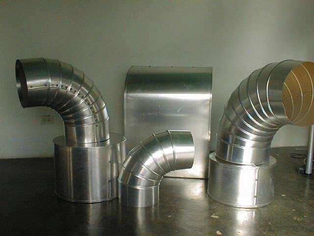 Conjunto de tubos de metal en forma de codo conectados a bases redondas, formando un sistema de ventilación o extracción en un entorno industrial.