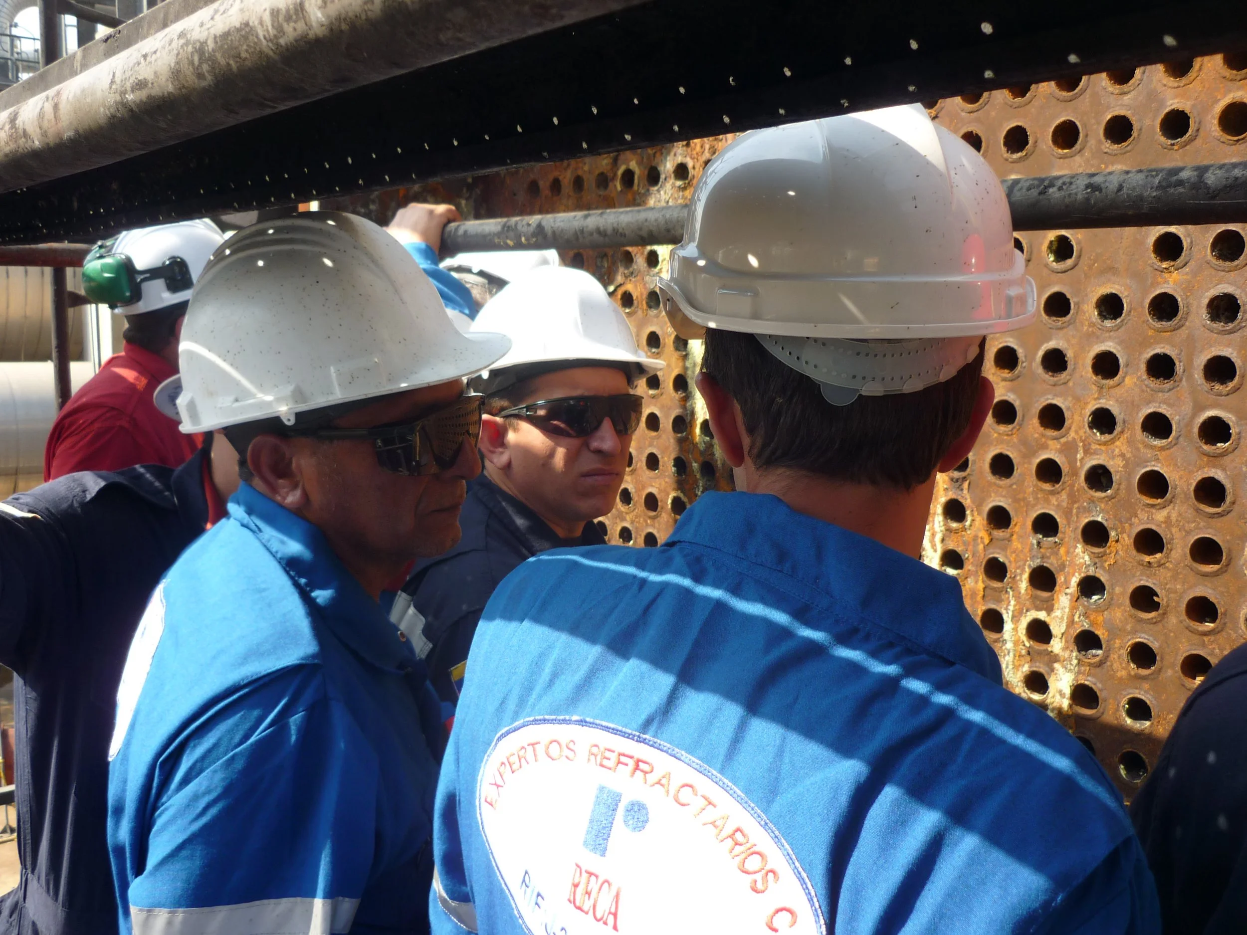 Grupo de ingenieros en uniformes de trabajo y cascos de seguridad inspeccionando intercambiadores