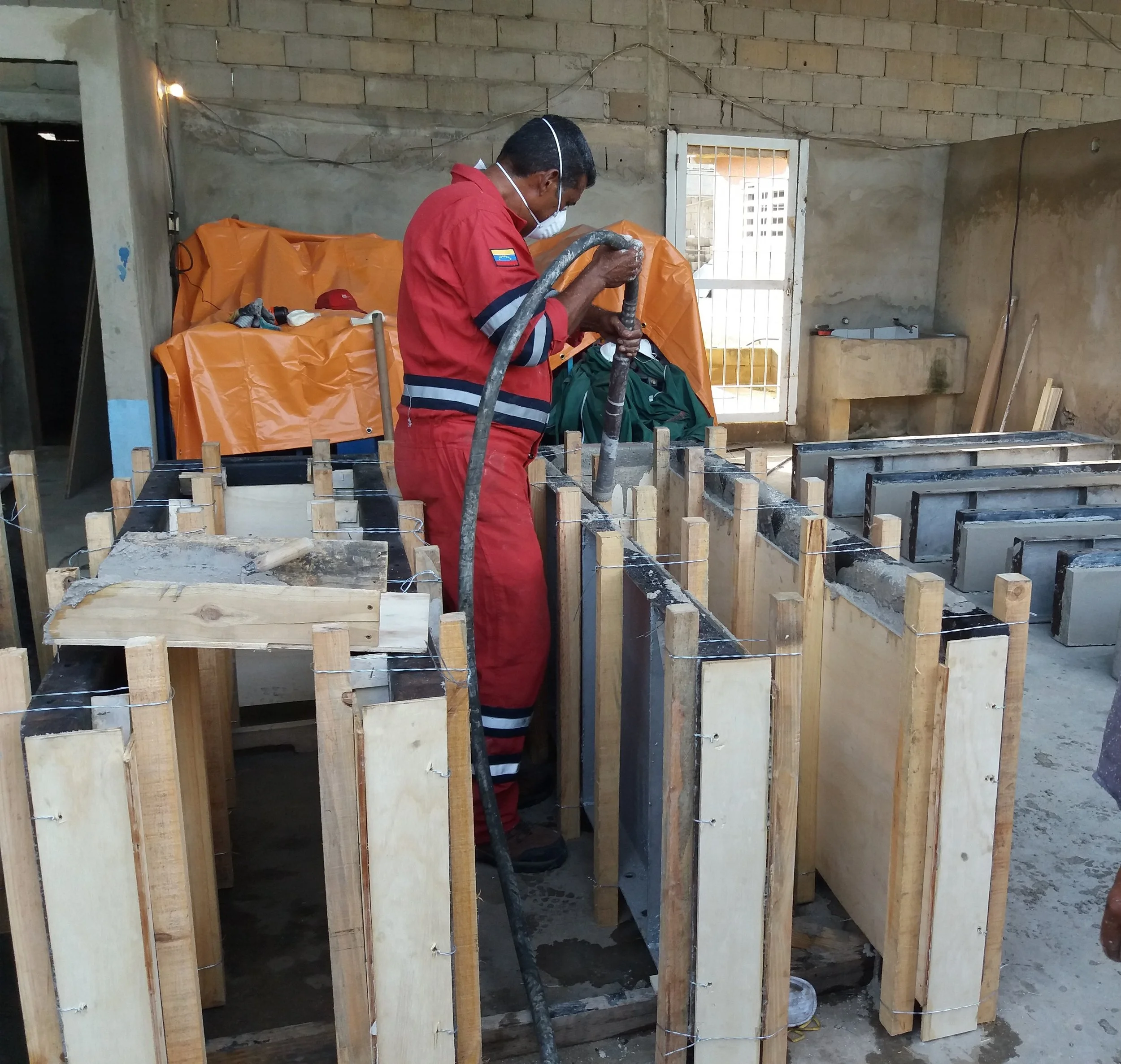 Un hombre en uniforme de bombero roji-blanco trabaja con una manguera de agua en una construcción de cimientos de ladrillos y madera.