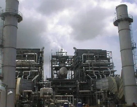 Vista de una planta industrial petrolera con tuberías y chimeneas, bajo un cielo nublado.