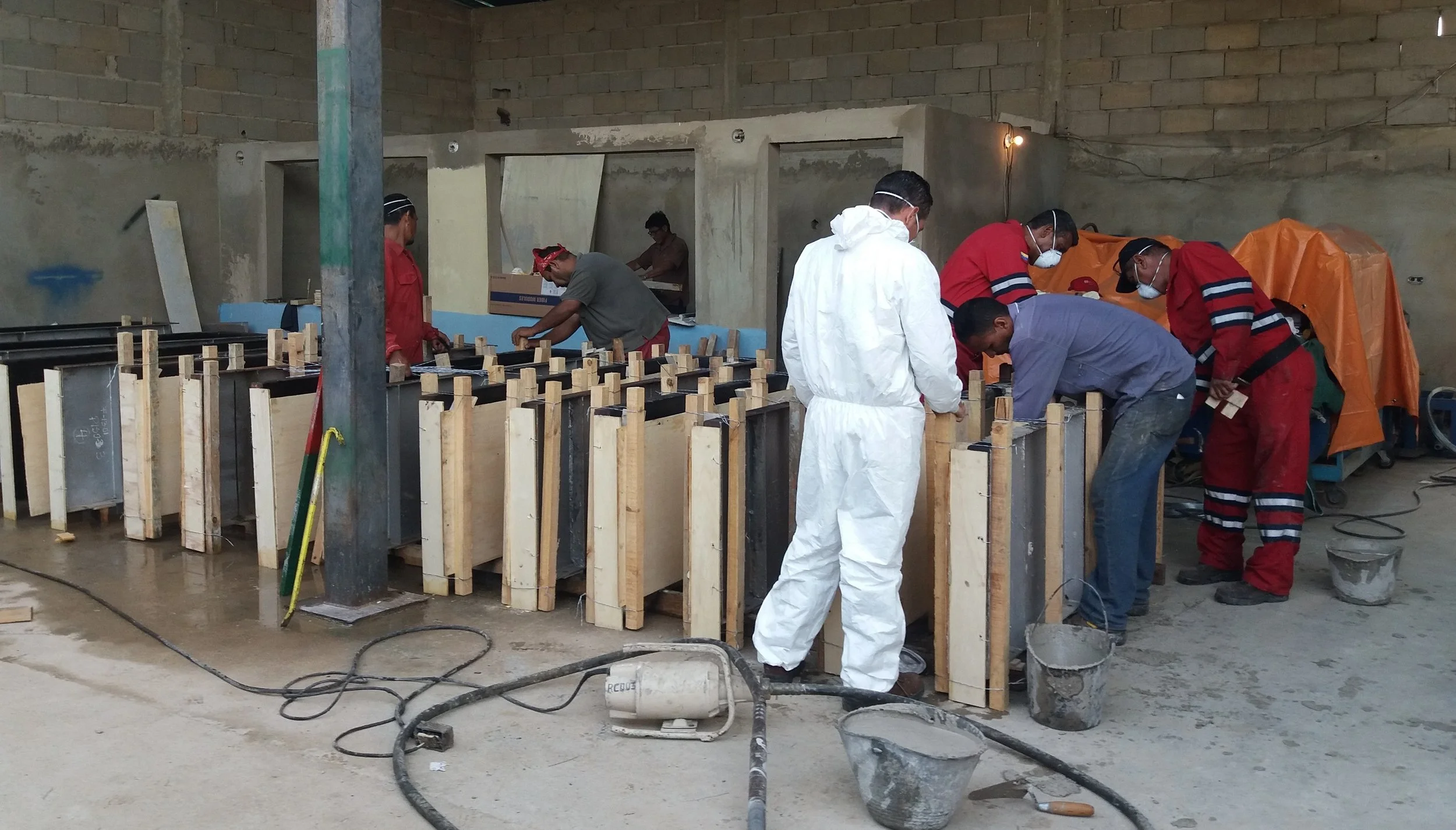 Personas trabajando en la construcción o fabricación en un taller, manipulando estructuras de concreto o madera.