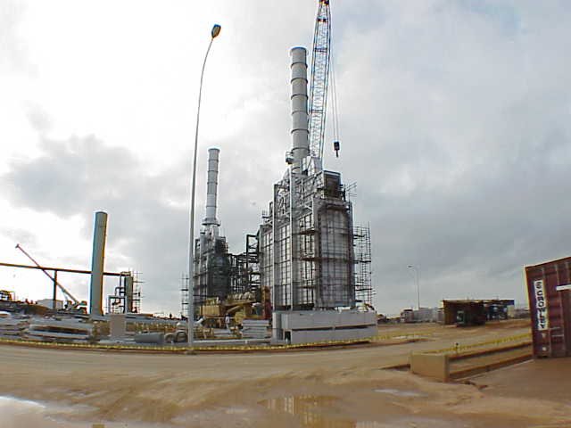 Planta industrial en construcción en refineria, maquinaria y equipo en un sitio de obra con suelo de tierra en un día nublado.