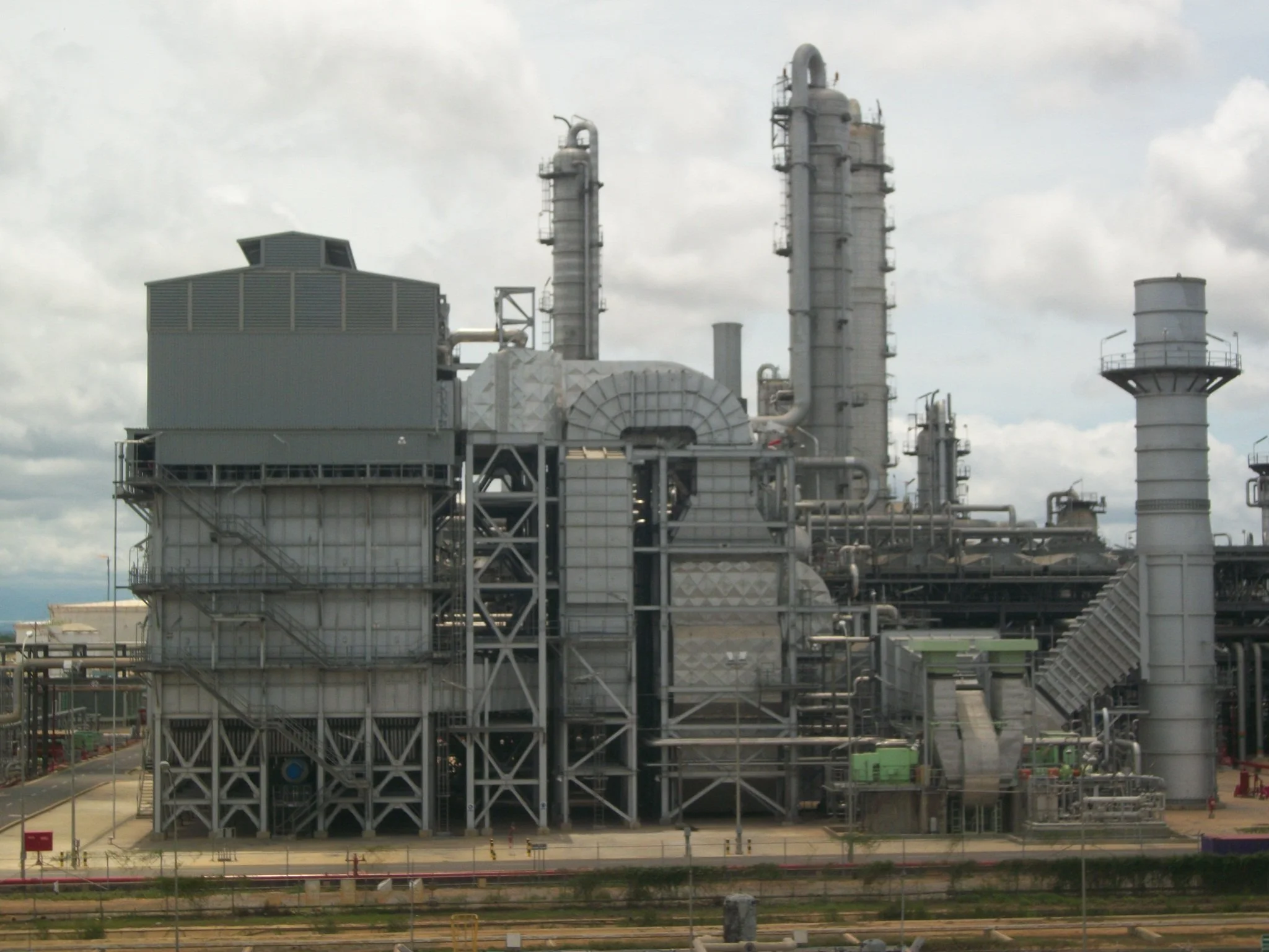 planta refineria petrolera  con varias estructuras metálicas y chimeneas contra un cielo nublado.