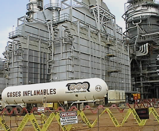 Planta industrial con un cilindro de gas inflamable en primer plano, rodeado de cinta de advertencia amarilla.