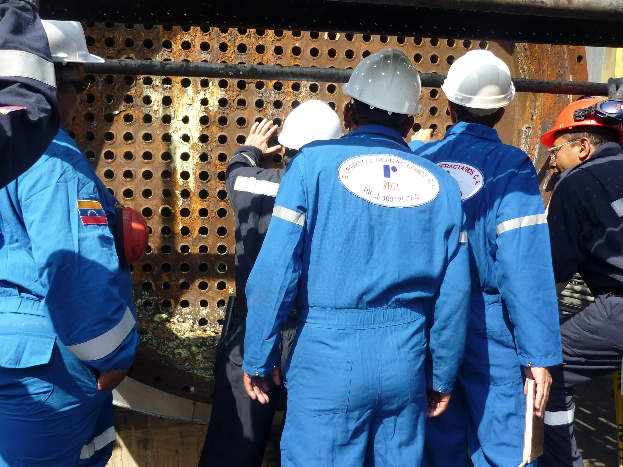 Grupo de trabajadores con uniformes de protección inspeccionando una estructura metálica oxidada en una obra de construcción o reparación.