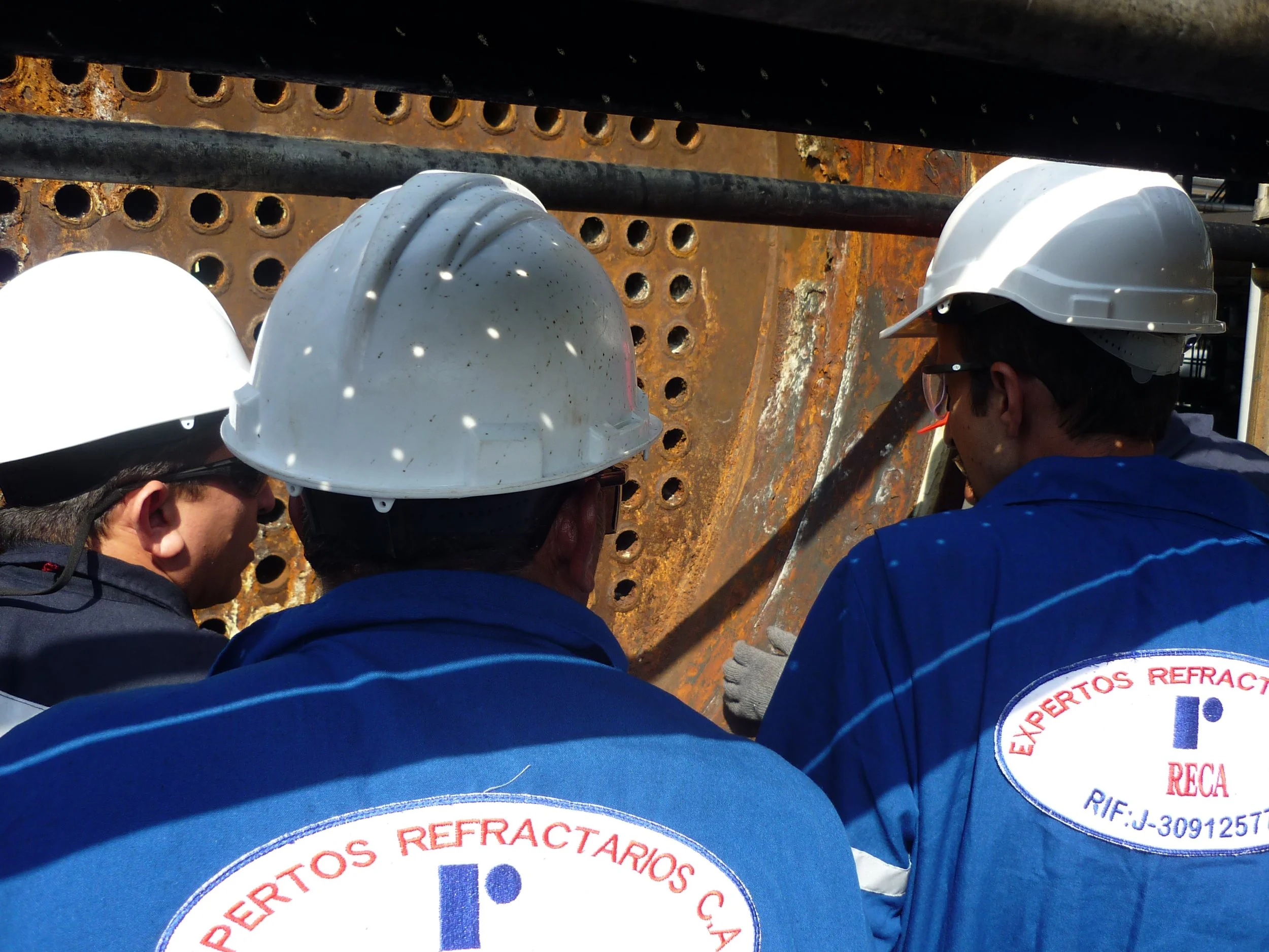 Grupo de ingenieros en uniformes de trabajo y cascos de seguridad inspeccionando intercambiadores