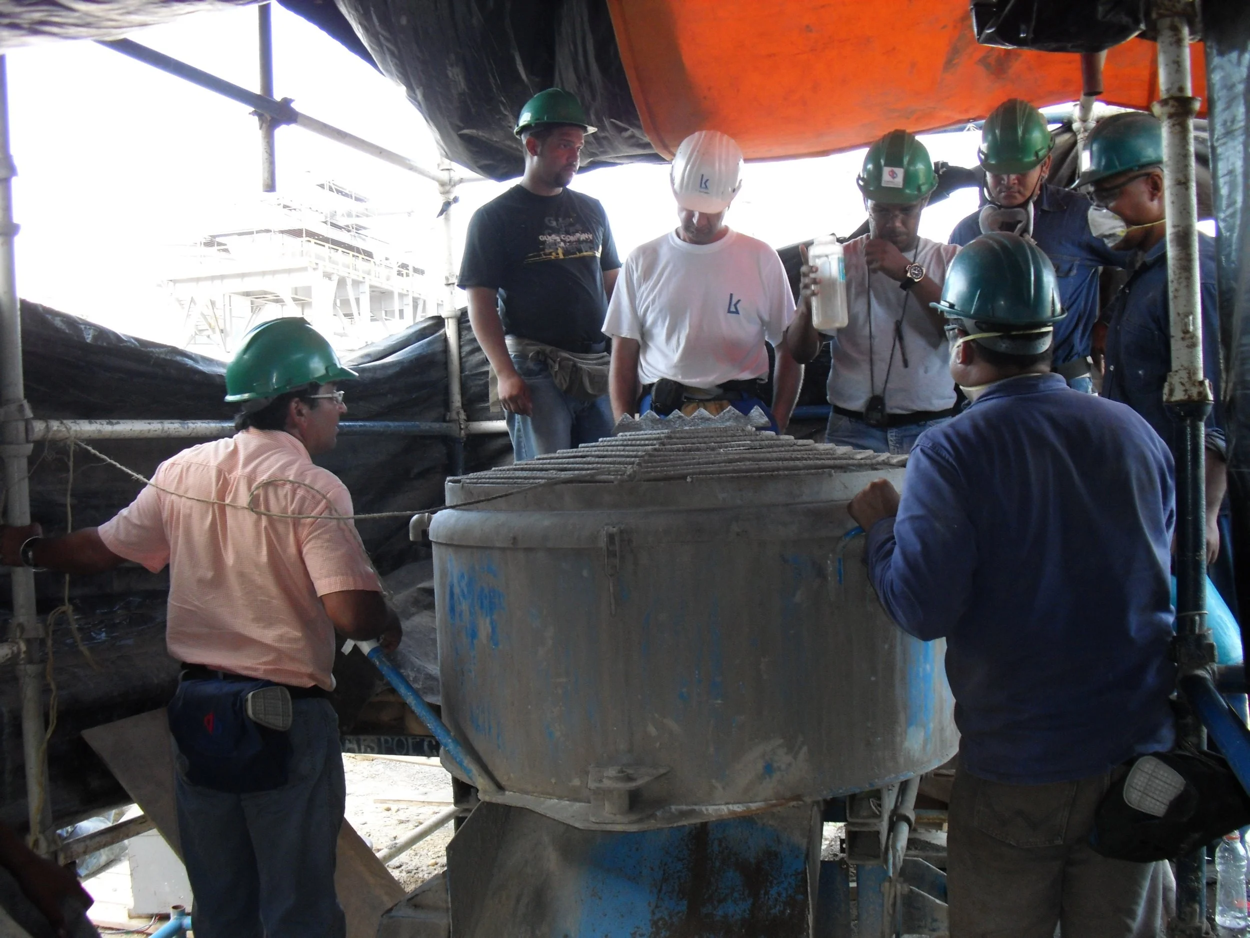 vaciado de reformador secundario. Trabajadores en uniformes y cascos de seguridad mezclando material refractario en una estructura de andamios