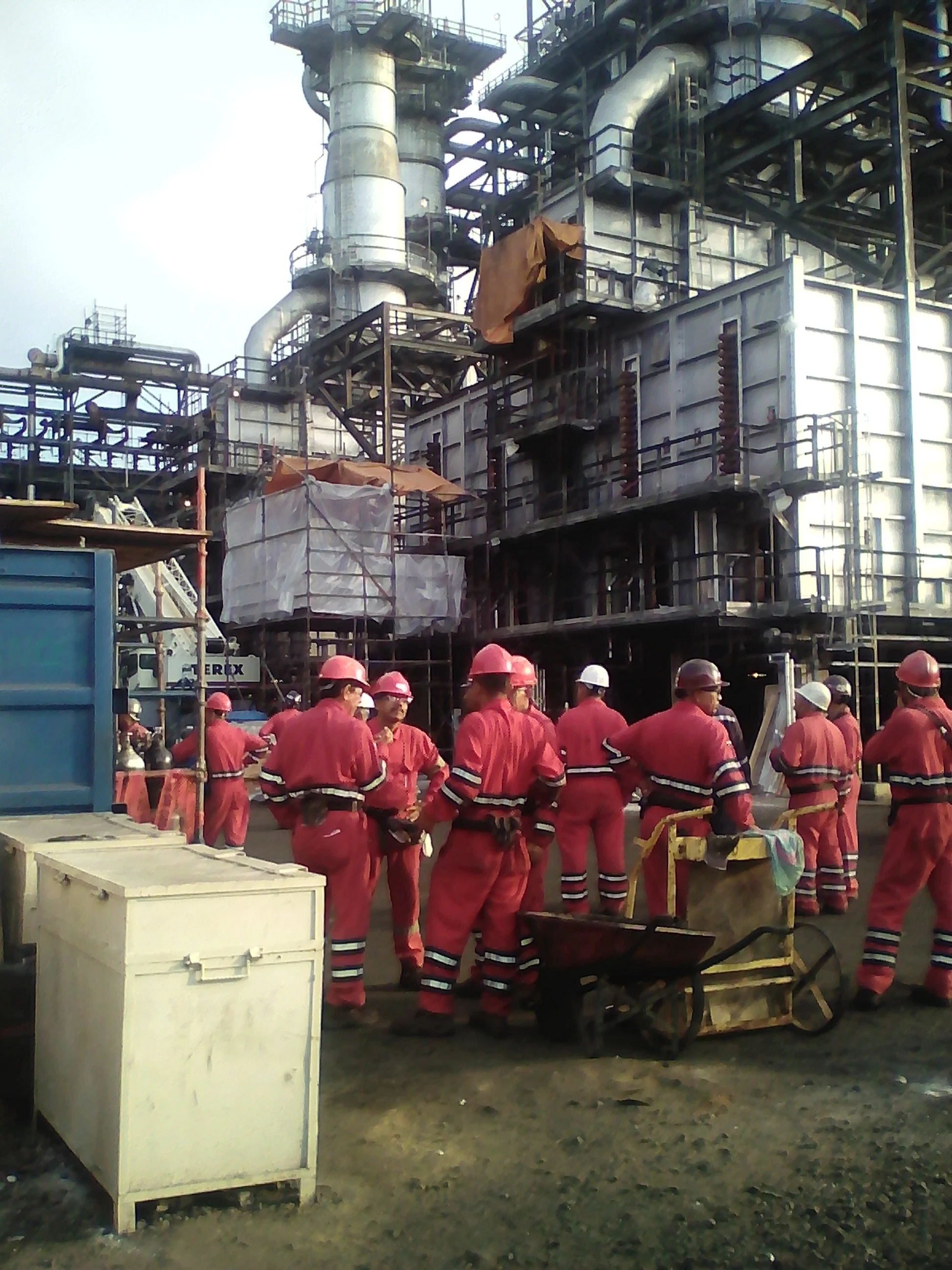 Trabajadores en uniforme rojo y cascos rojos operan maquinaria en una refineria.