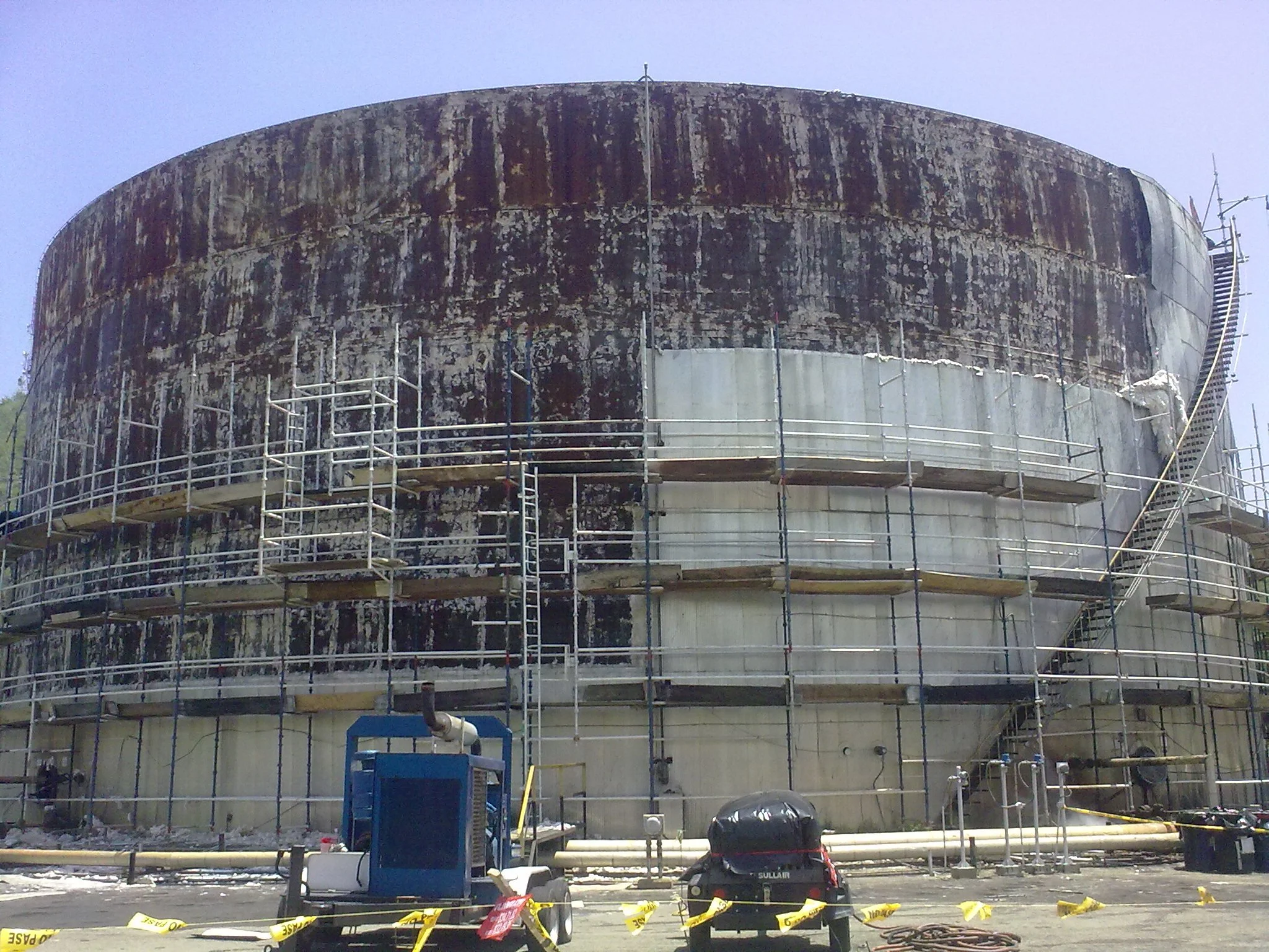 Rehabilitacion. Trabajadores con casco en una estructura de andamios alrededor de tanque de almacenamiento petrolero