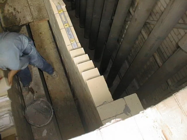 trabajador en pasillo con paredes de ladrillos, colocando ladrillos refractarios  